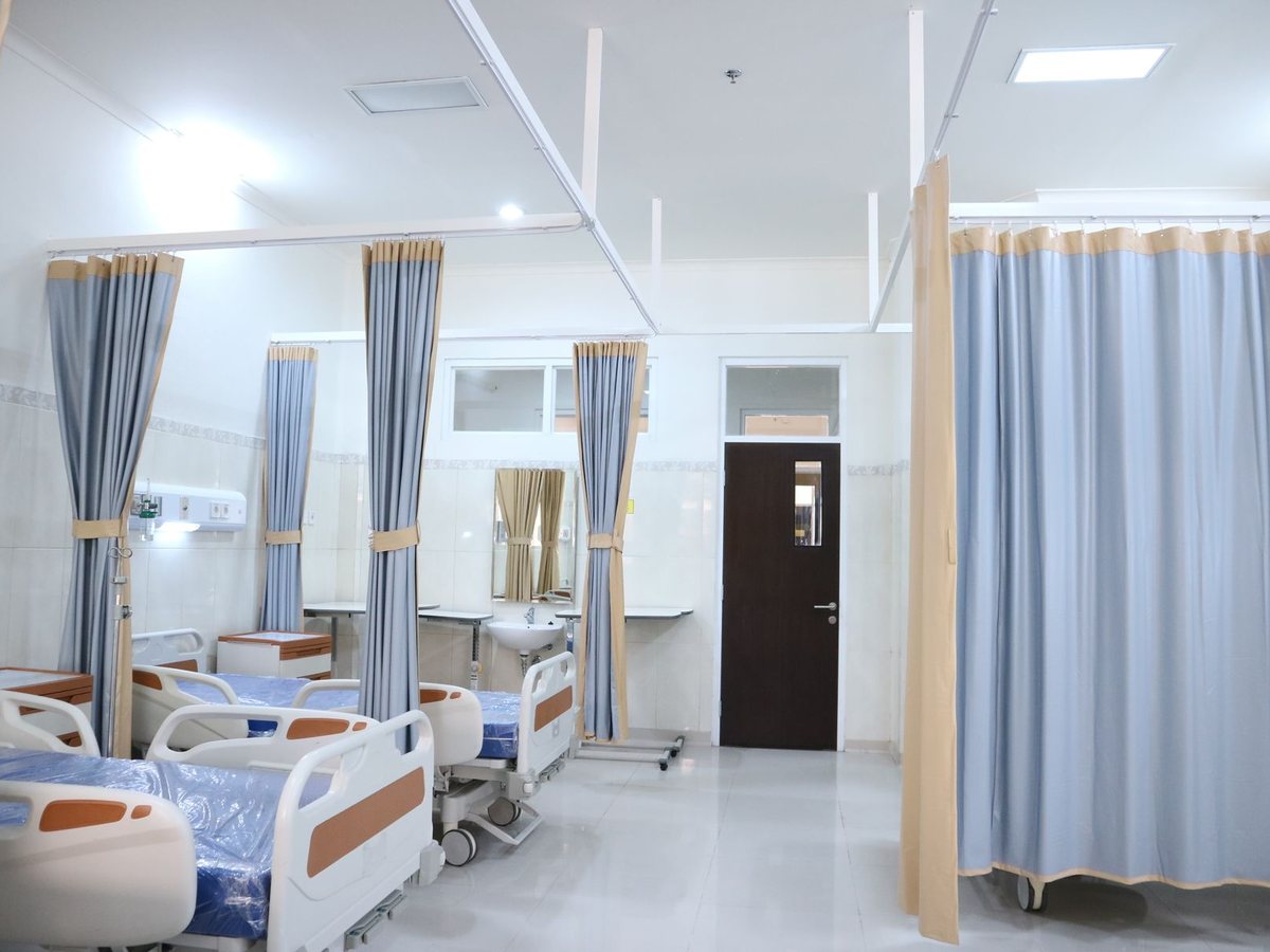 A bright, empty modern hospital ward with made beds and privacy curtains